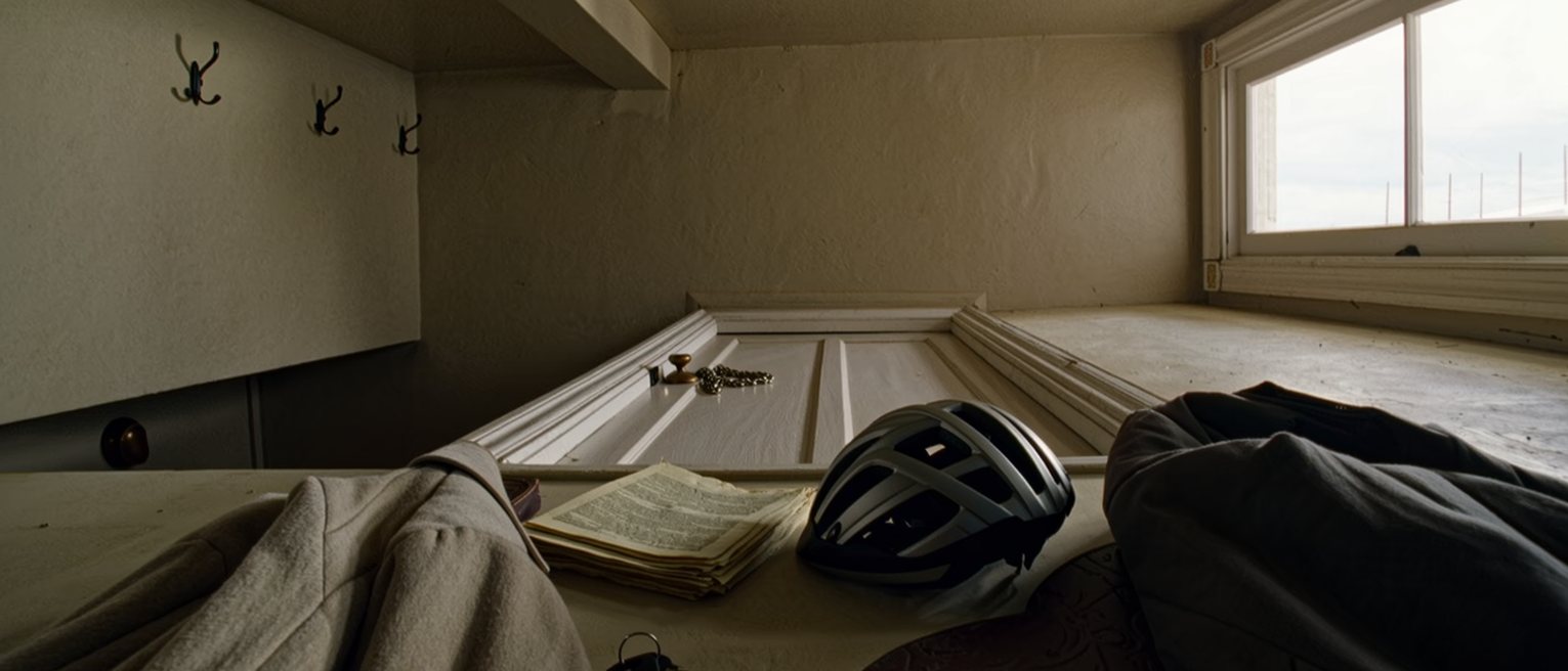 a hall seen close with a coat on the hook, a bicycle helmet, a folder of papers on the console and a set of keys, the door with its chain soft behind
