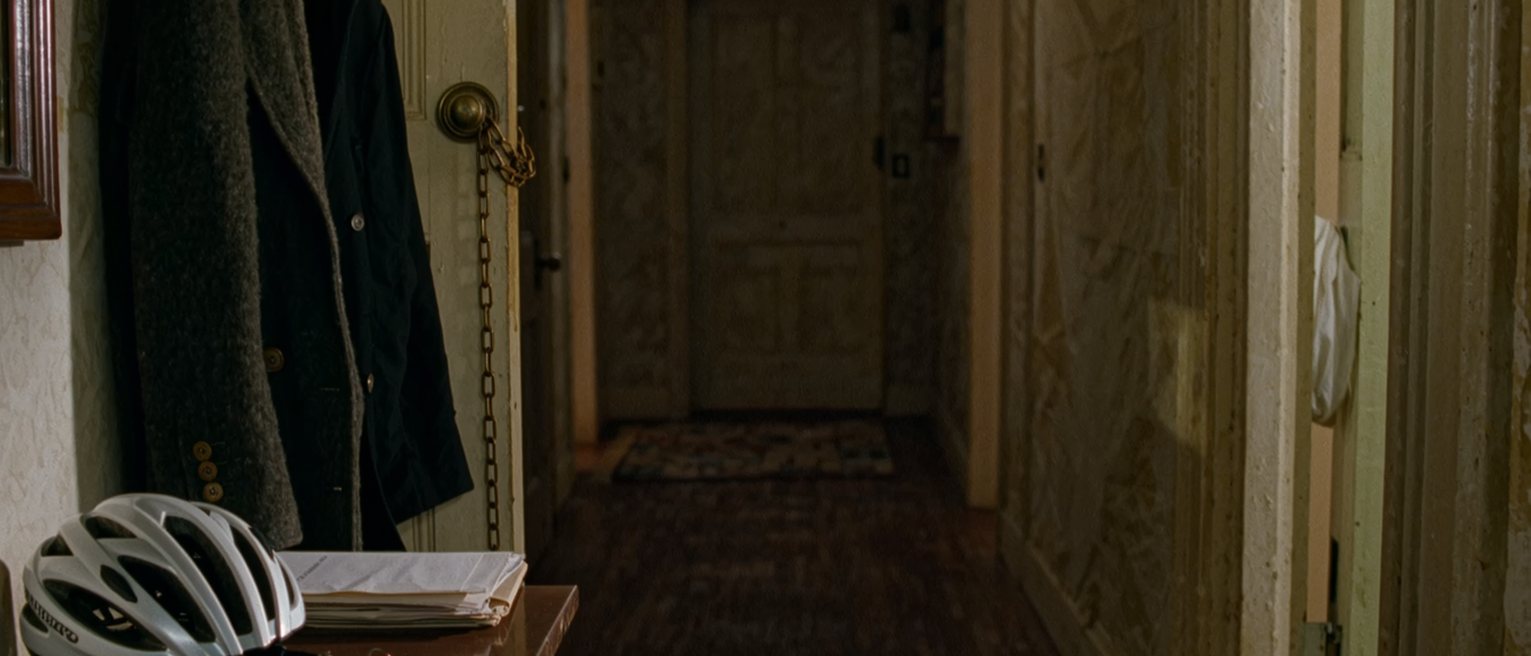a hall seen close with a coat on the hook, a bicycle helmet, a folder of papers on the console and a set of keys, the door with its chain soft behind