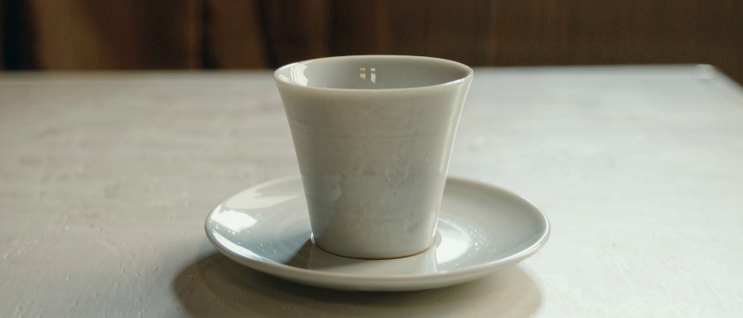 one cup and one saucer set out on a clean table, the cup turned upright