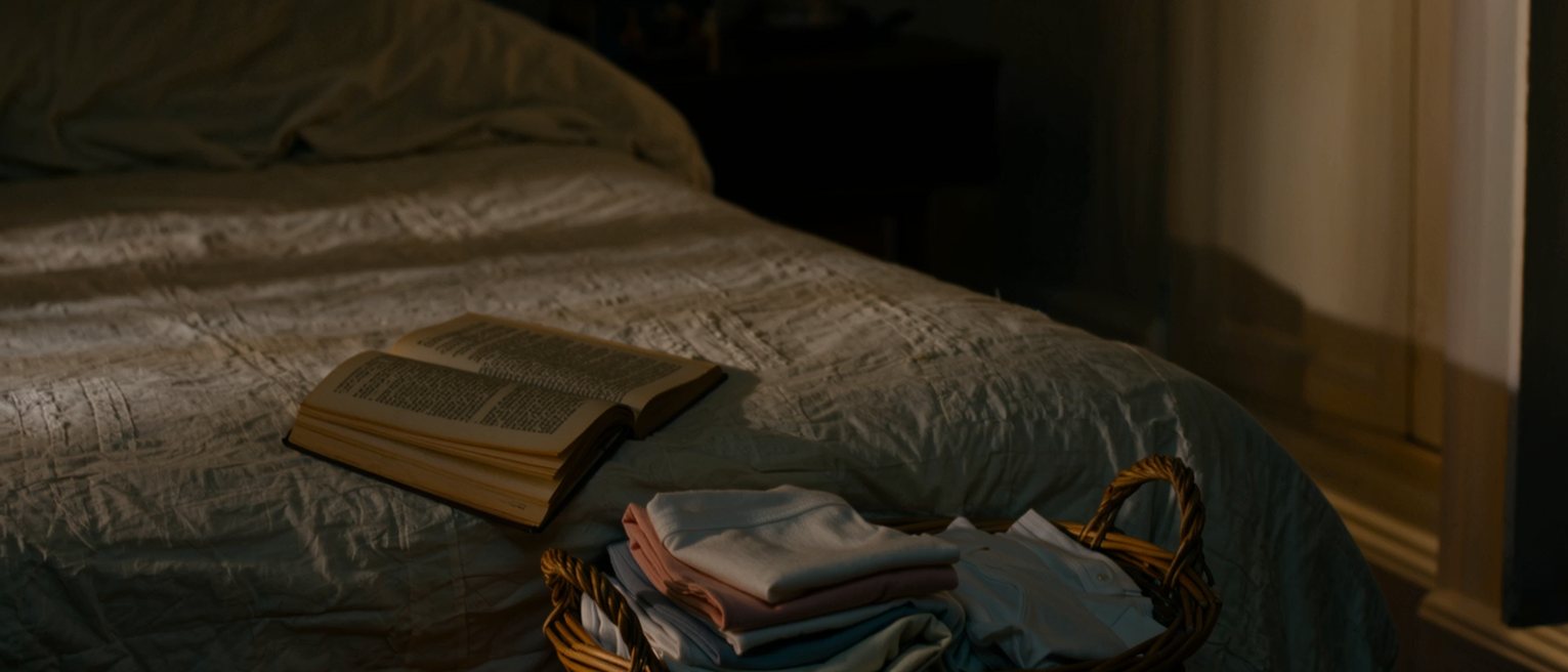 a bedroom with a novel left open face down on the pillow and a basket of folded laundry set on the end of the bed