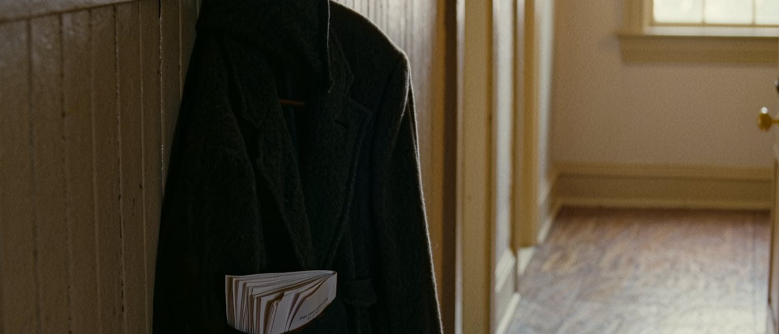 a hall with a coat on the hook and a printed sheaf of pages folded into the coat pocket, only the corner showing