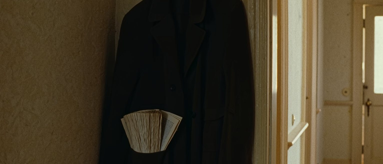a hall with a coat on the hook and a printed sheaf of pages folded into the coat pocket, only the corner showing