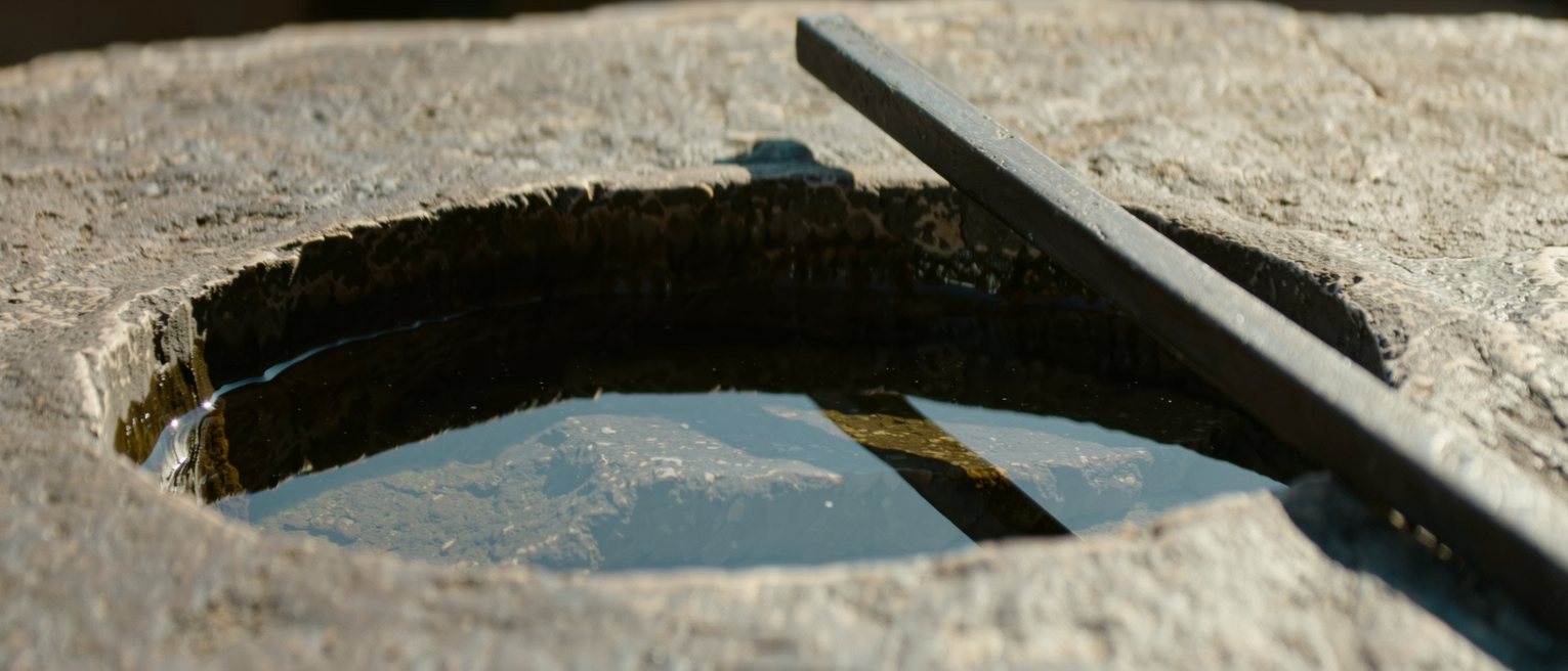 a blacksmith's quench tub of still water with a finished iron bar on the stone beside it