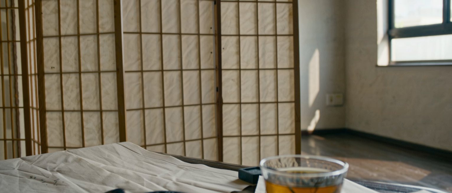 a low desk seen close with a brush, an ink stone and a sheet of calligraphy drying, a cup of oolong tea gone cold and a folded note, the paper screen soft behind