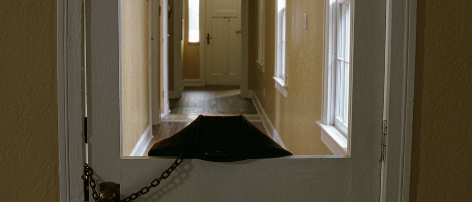 a front door with the chain on and a coat hung on the inside of it, the hall behind tidy and unhurried