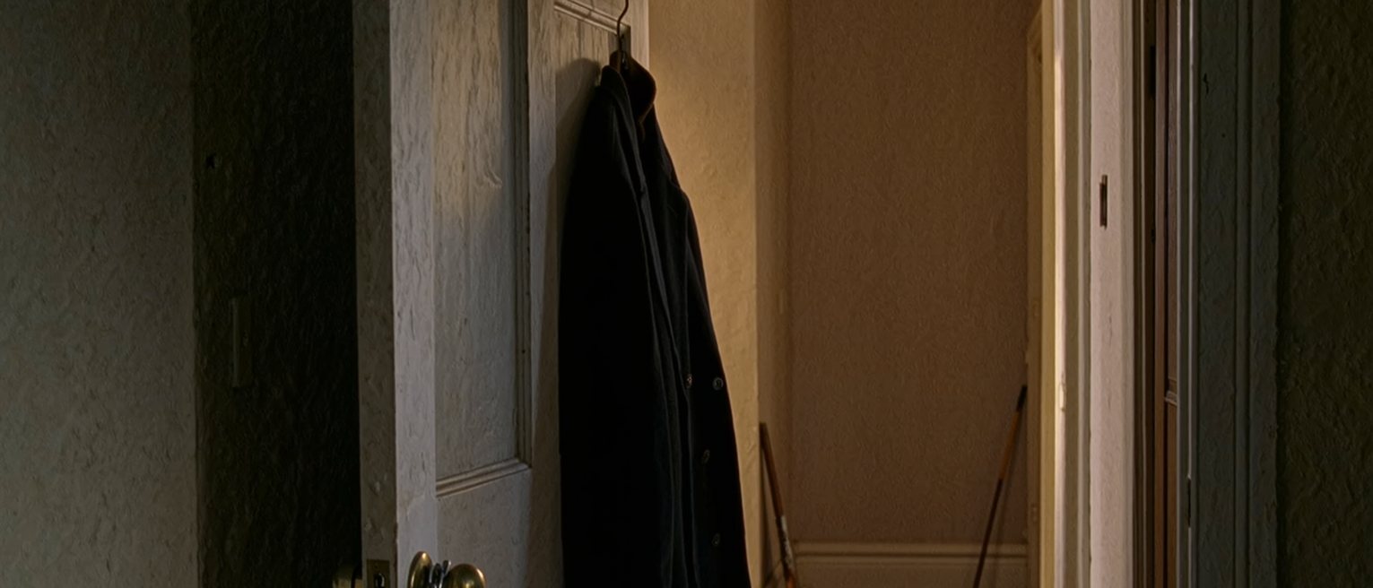 a front door with the chain on and a coat hung on the inside of it, the hall behind tidy and unhurried