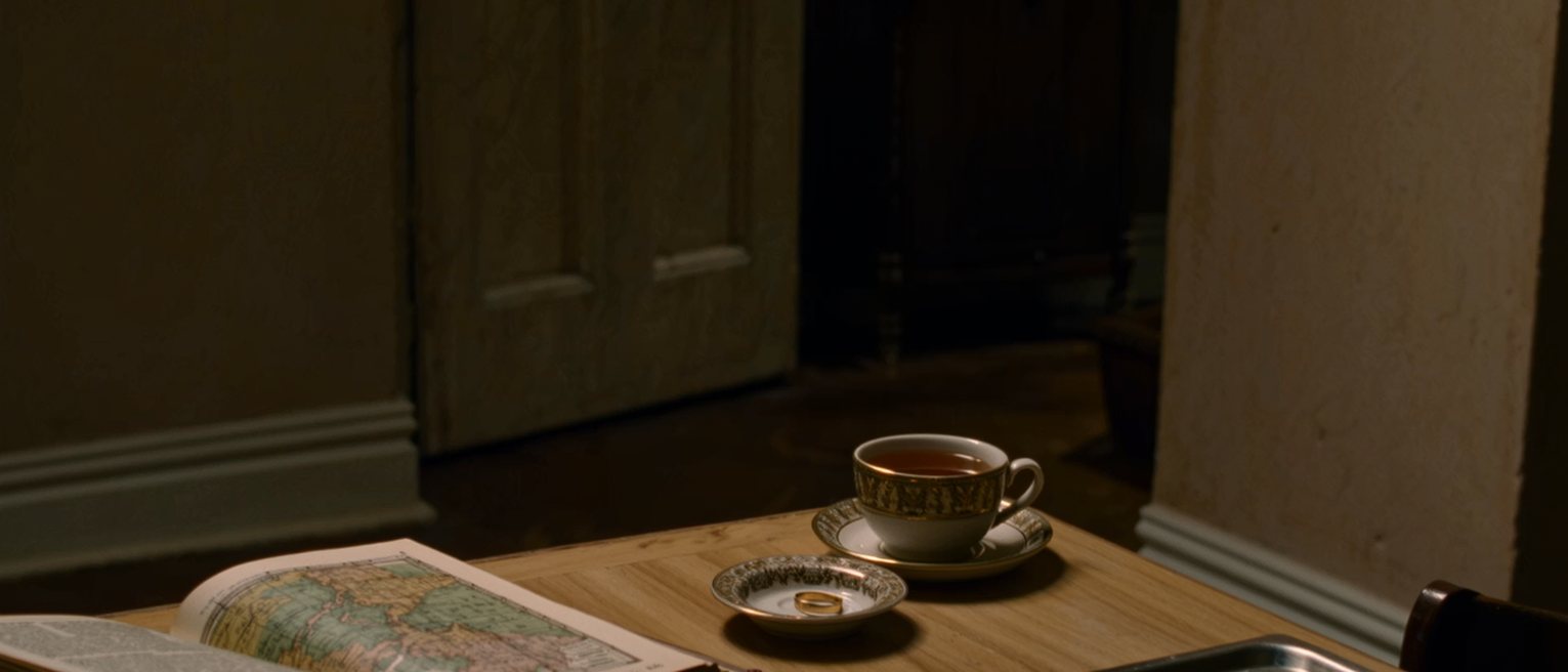 a kitchen table with an atlas open at a page far from home and a cup of tea beside it, a pair of rings in a dish by the sink