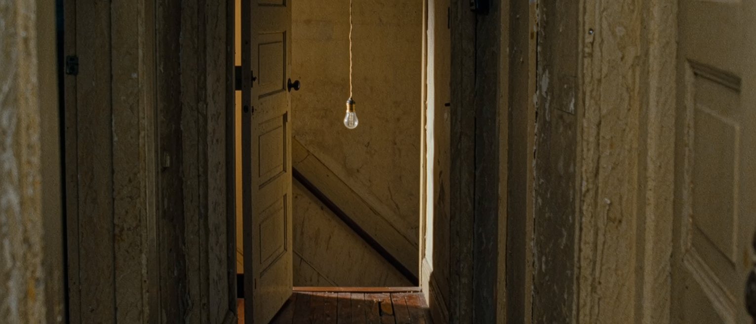 a narrow stair landing in an apartment building with two front doors facing each other across it, both closed, a single bare bulb on a cord between them