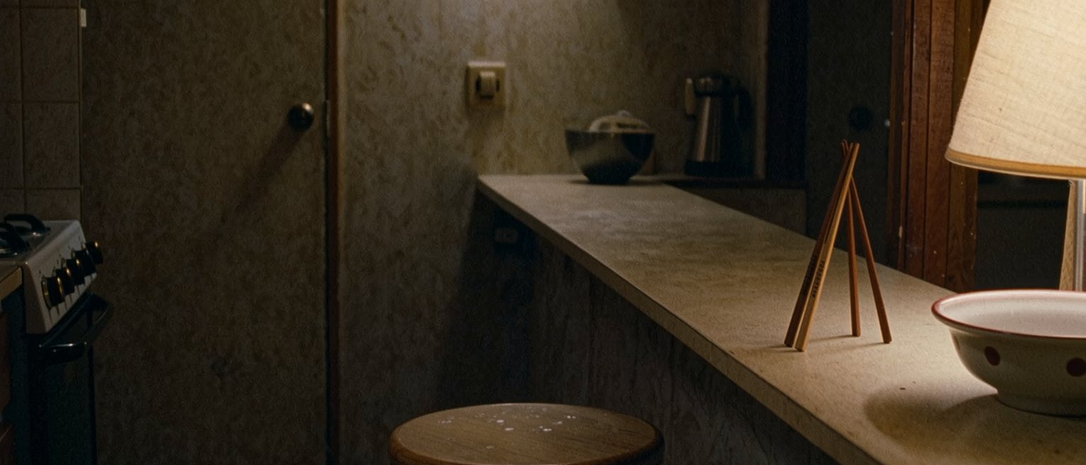 a narrow kitchen counter in a small flat with two stools, one pushed in and one left out, a cleared bowl and a pair of chopsticks standing at each