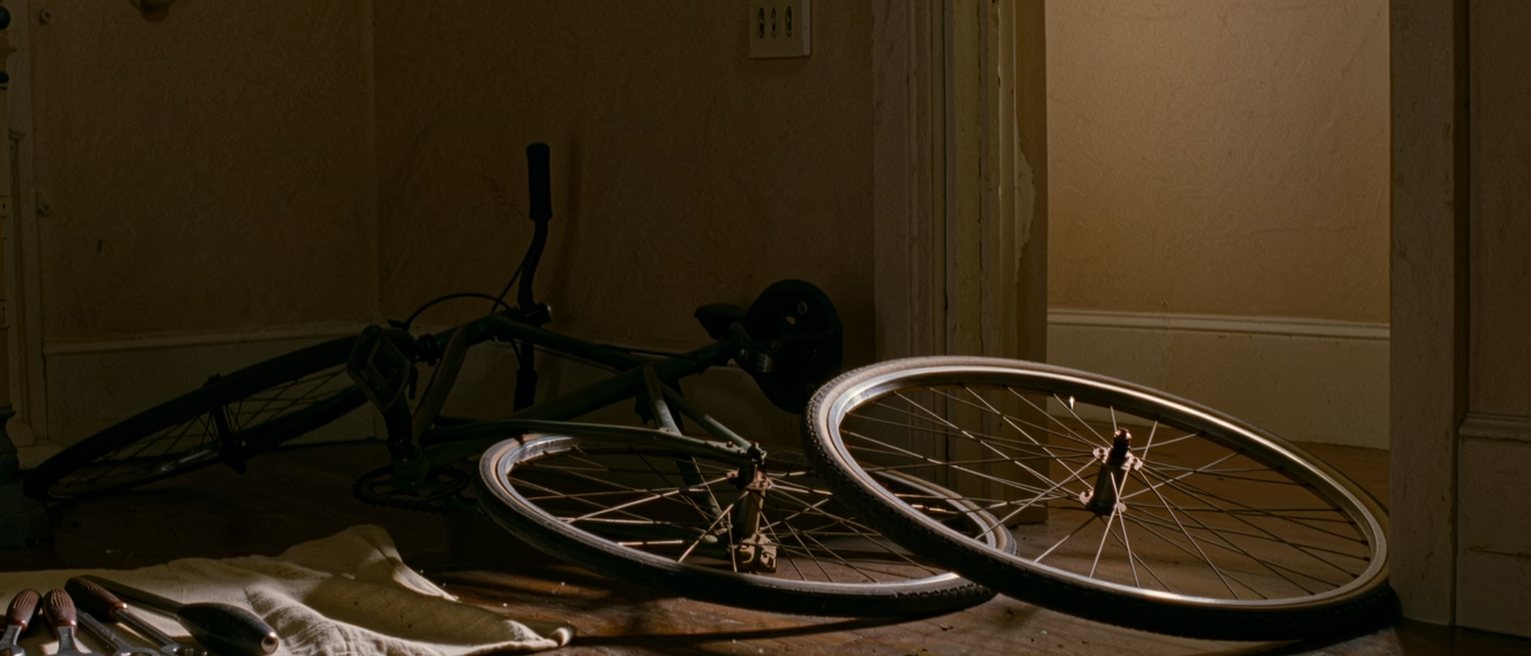 a hall with a bicycle leaning against the wall, its front wheel off and a borrowed set of tools laid out on a cloth beside it