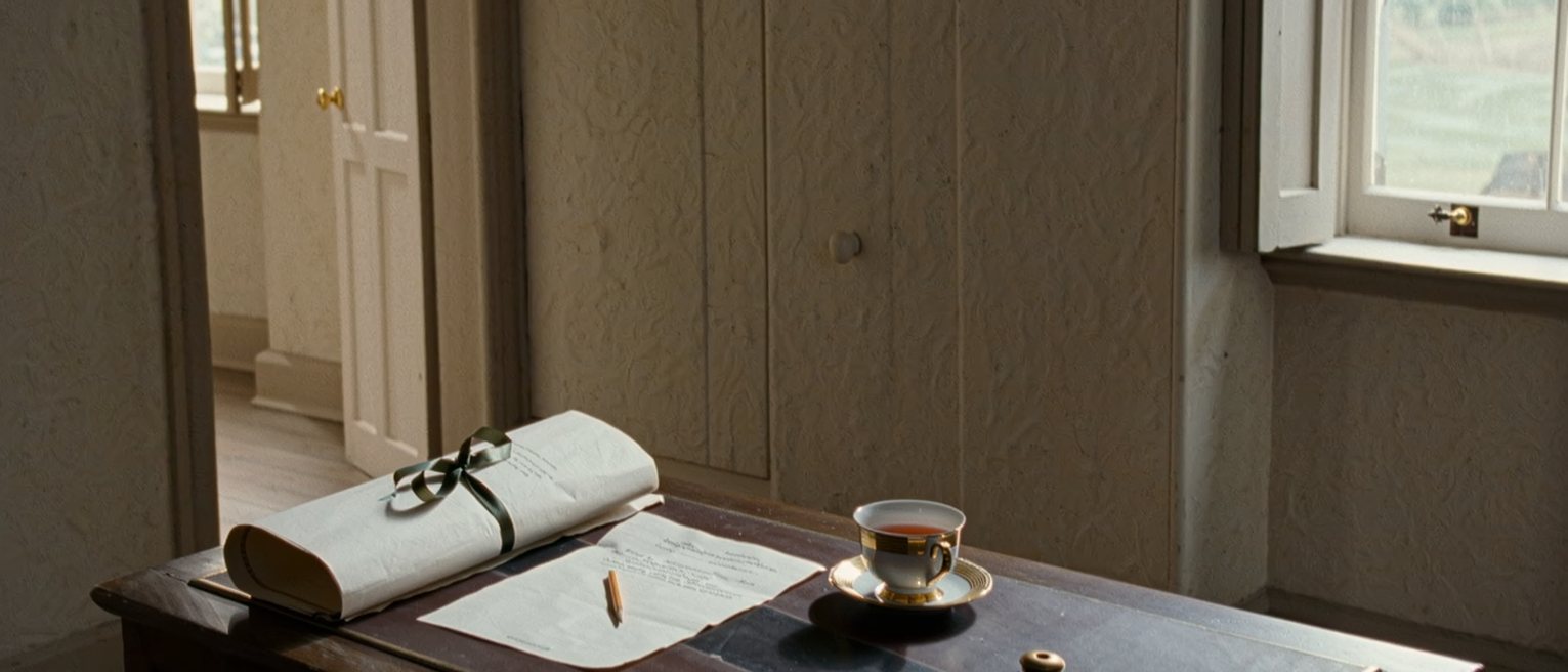 a writing desk seen close with a manuscript tied in ribbon beside a contract with a copyright line marked in pencil, a cup of tea and an inkwell, the window with snow on the sill soft behind