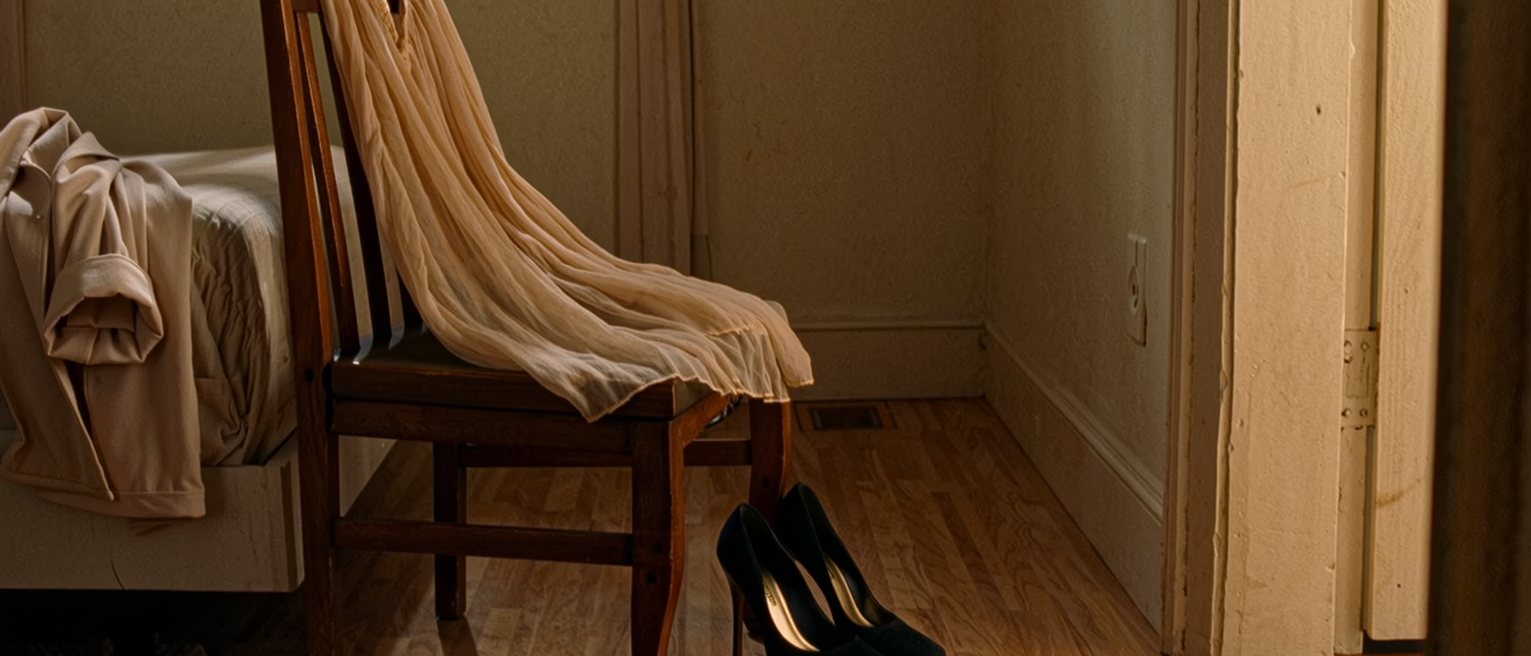 a bedroom chair with a dress and its heels set out ready, and on the bed beside it a worn cotton robe just taken off