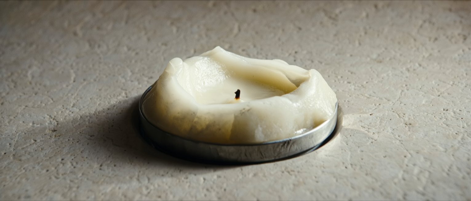 a candle burned down to a stub in its holder, the wax run over the edge
