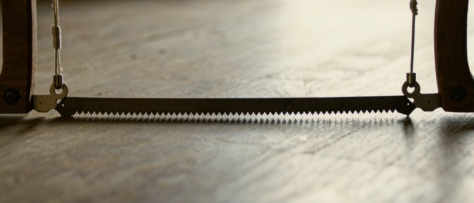 a carpenter's frame saw with its tensioning cord twisted tight, the blade held rigid by the span across the frame