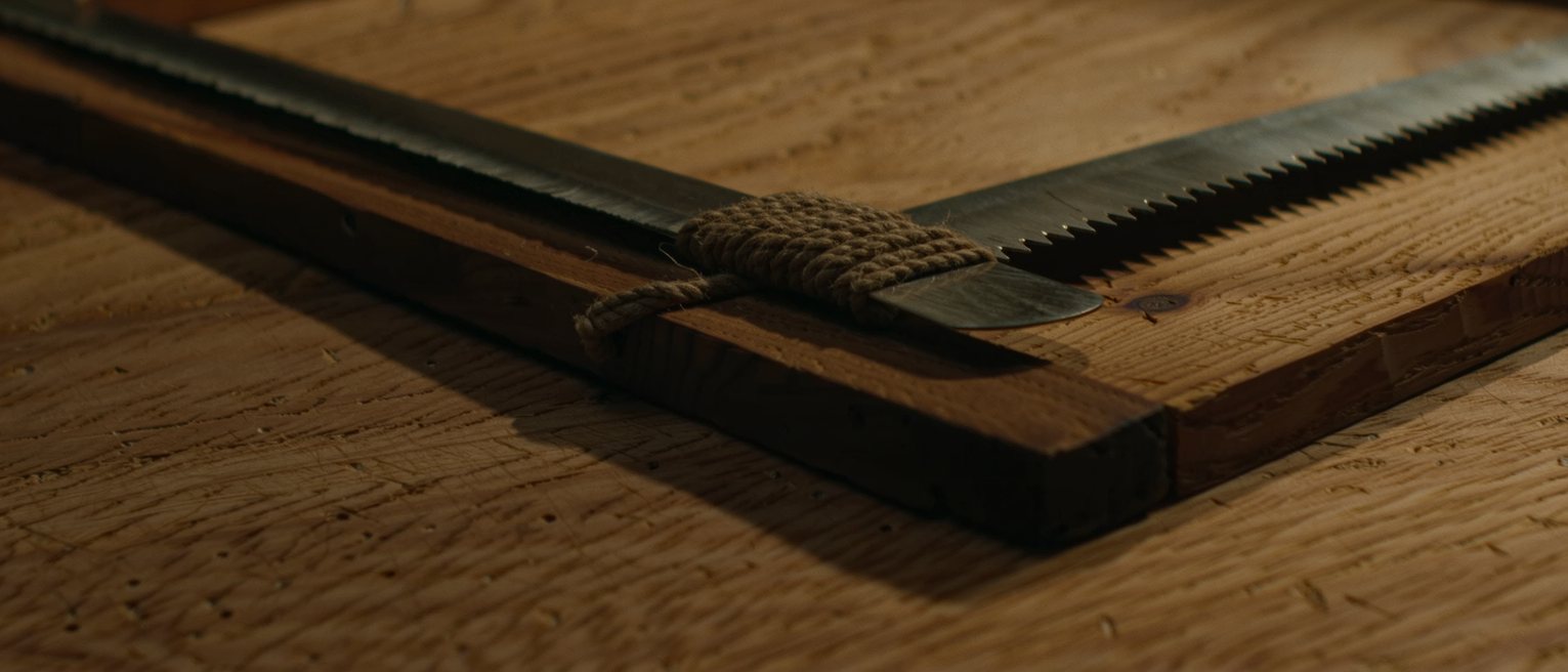 a carpenter's frame saw with its tensioning cord twisted tight, the blade held rigid by the span across the frame