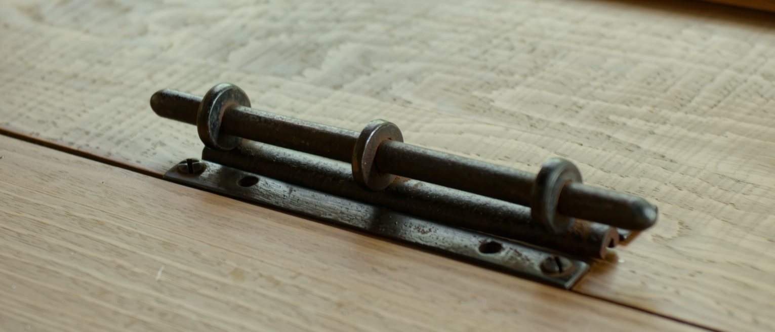 an iron thumb latch mounted on the timber of a door, its bar lying dropped into the catch where its own weight has left it