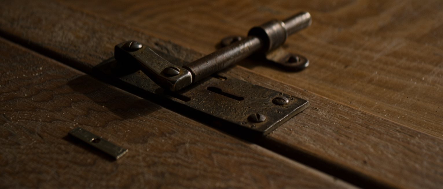 an iron thumb latch mounted on the timber of a door, its bar lying dropped into the catch where its own weight has left it