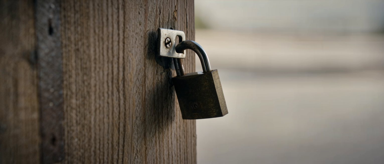 a heavy padlock closed through the staple of an iron hasp on a timber door, the shackle fully seated