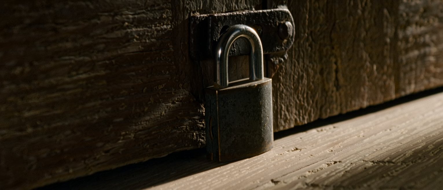 a heavy padlock closed through the staple of an iron hasp on a timber door, the shackle fully seated