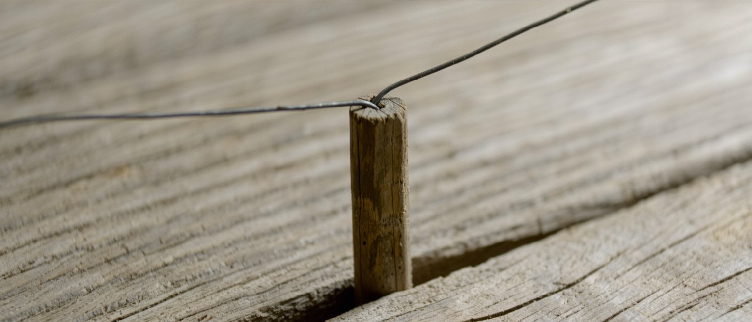 a single wooden fence post driven into the ground with one wire strained to it