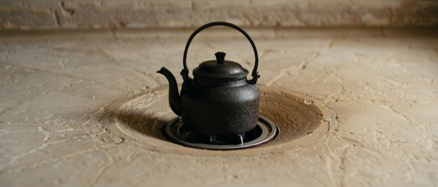 a cast-iron kettle standing off the heat on a stone hearth, its lid closed