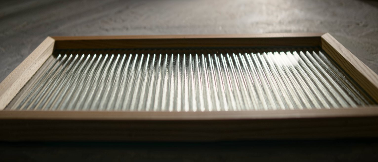 a pane of reeded glass in a wooden frame, its vertical flutes catching the light one after another