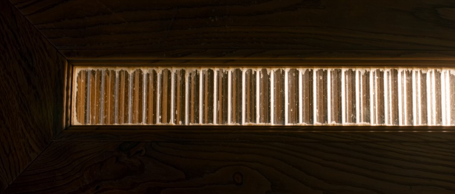 a pane of reeded glass in a wooden frame, its vertical flutes catching the light one after another