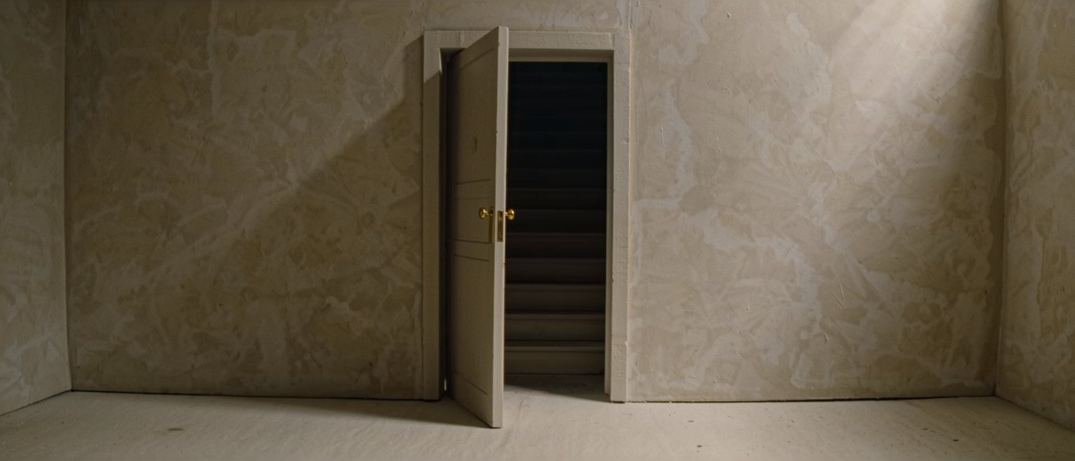a doorway left ajar onto a dark stair, the gap no wider than a hand