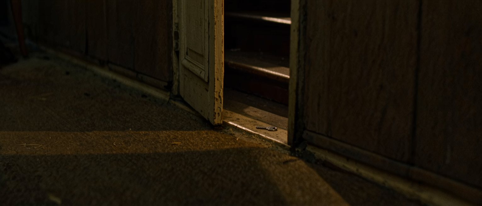 a doorway left ajar onto a dark stair, the gap no wider than a hand