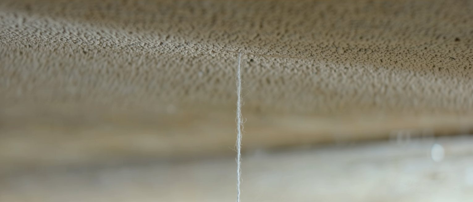 a single fine thread hung from a beam, hanging dead straight and still