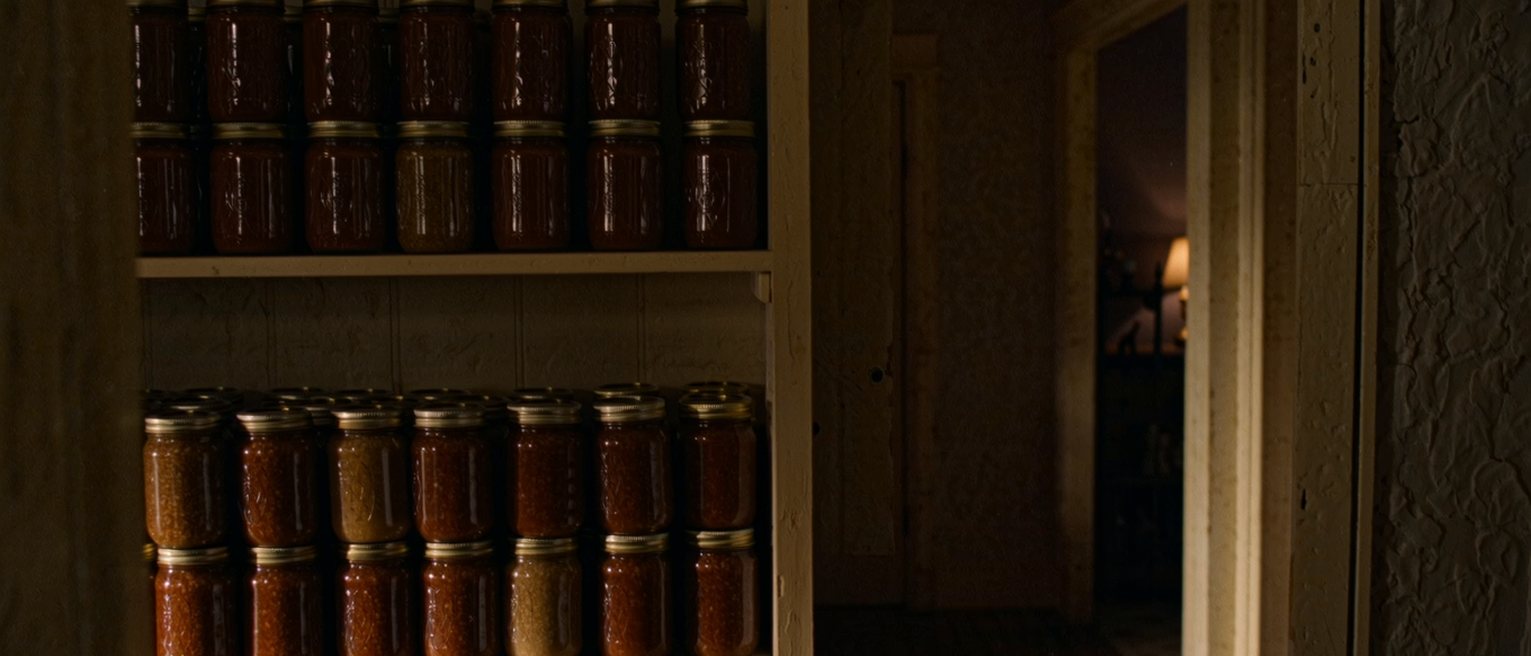 a pantry shelf stacked with identical jars in identical rows, every jar still full and not one of them opened