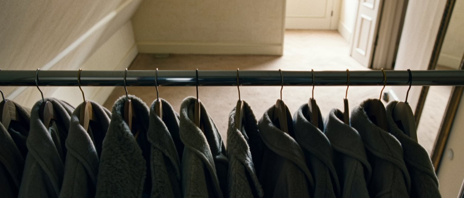 a wardrobe rail at home hung with near-identical coats, all one size, every hanger turned the same way