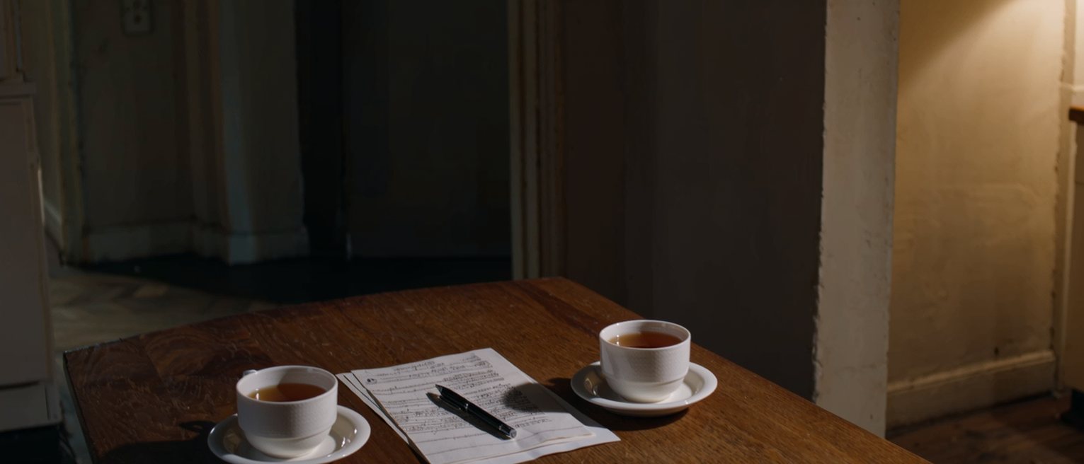 a kitchen table with a folded written agreement lying between two cups, a pen laid on top of it, the tea poured for both