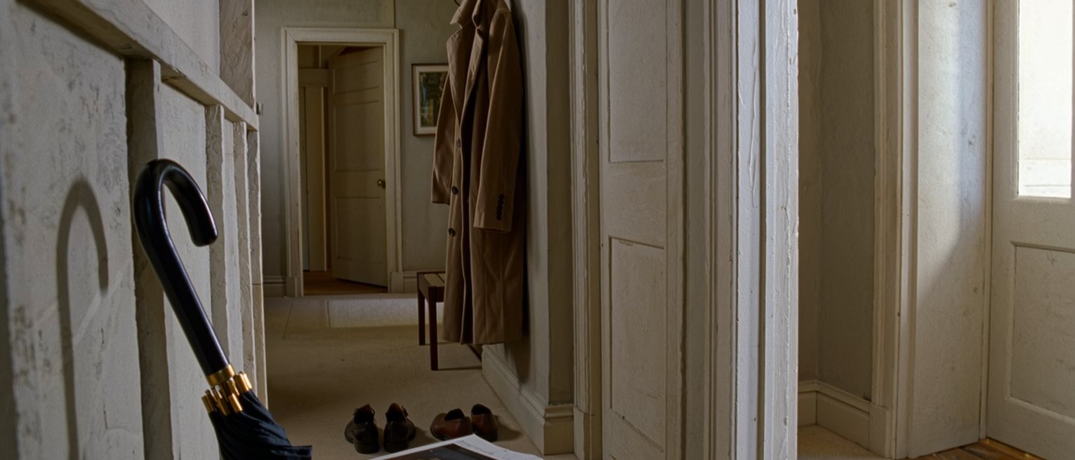 a hall seen close: one pair of shoes lined up on the mat, one coat on the hook, one umbrella in the stand and a stack of paperbacks on the hall table, nothing belonging to anyone else