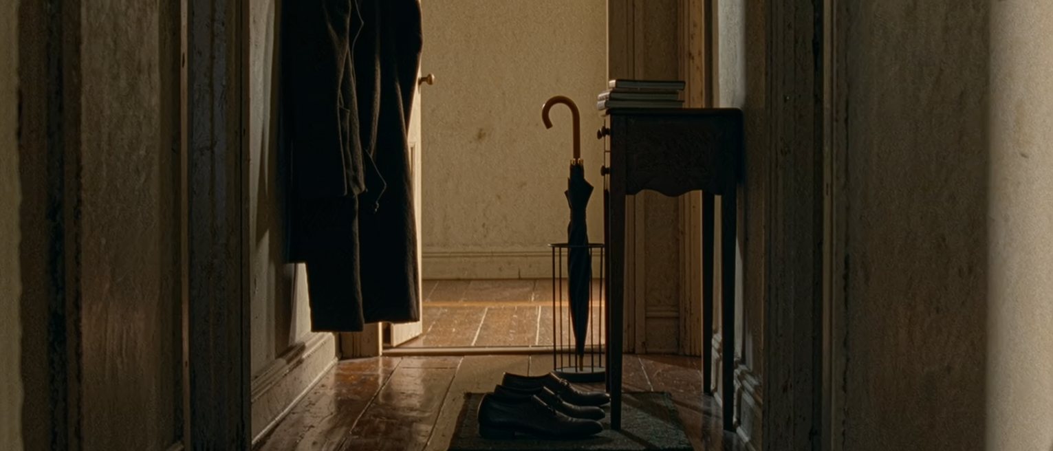 a hall seen close: one pair of shoes lined up on the mat, one coat on the hook, one umbrella in the stand and a stack of paperbacks on the hall table, nothing belonging to anyone else