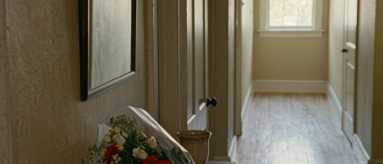 a hall table with a bunch of flowers still in their paper, not yet put in water, beside a vase left empty