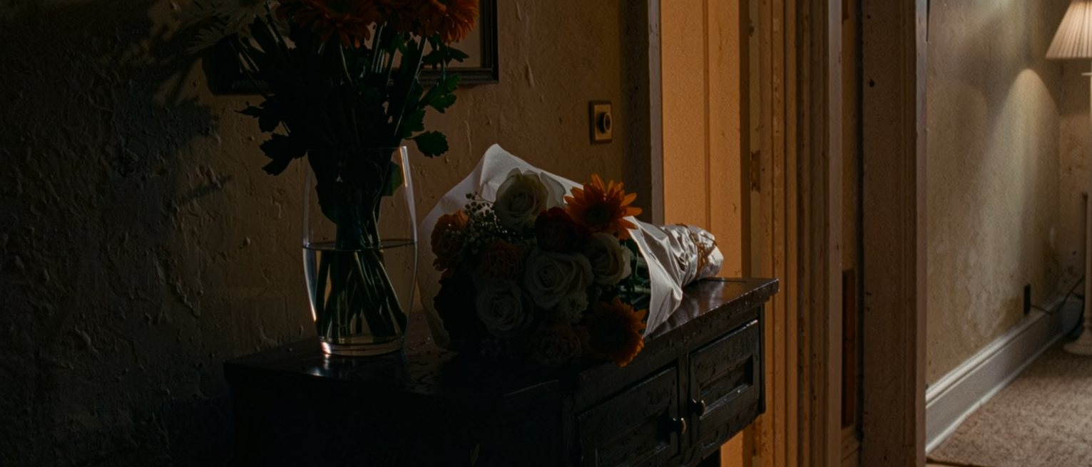 a hall table with a bunch of flowers still in their paper, not yet put in water, beside a vase left empty