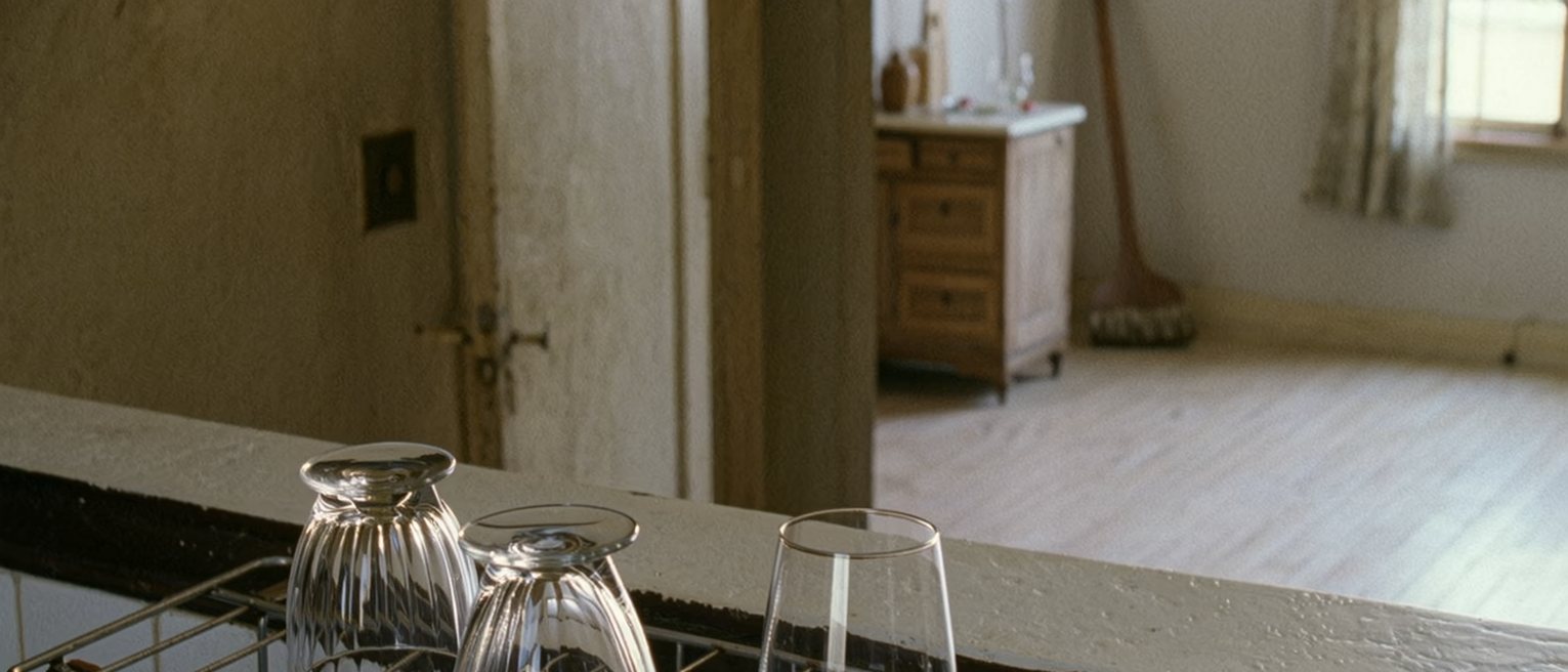 a kitchen with one wine glass washed and upturned on the rack and a second glass, still full, left on the counter