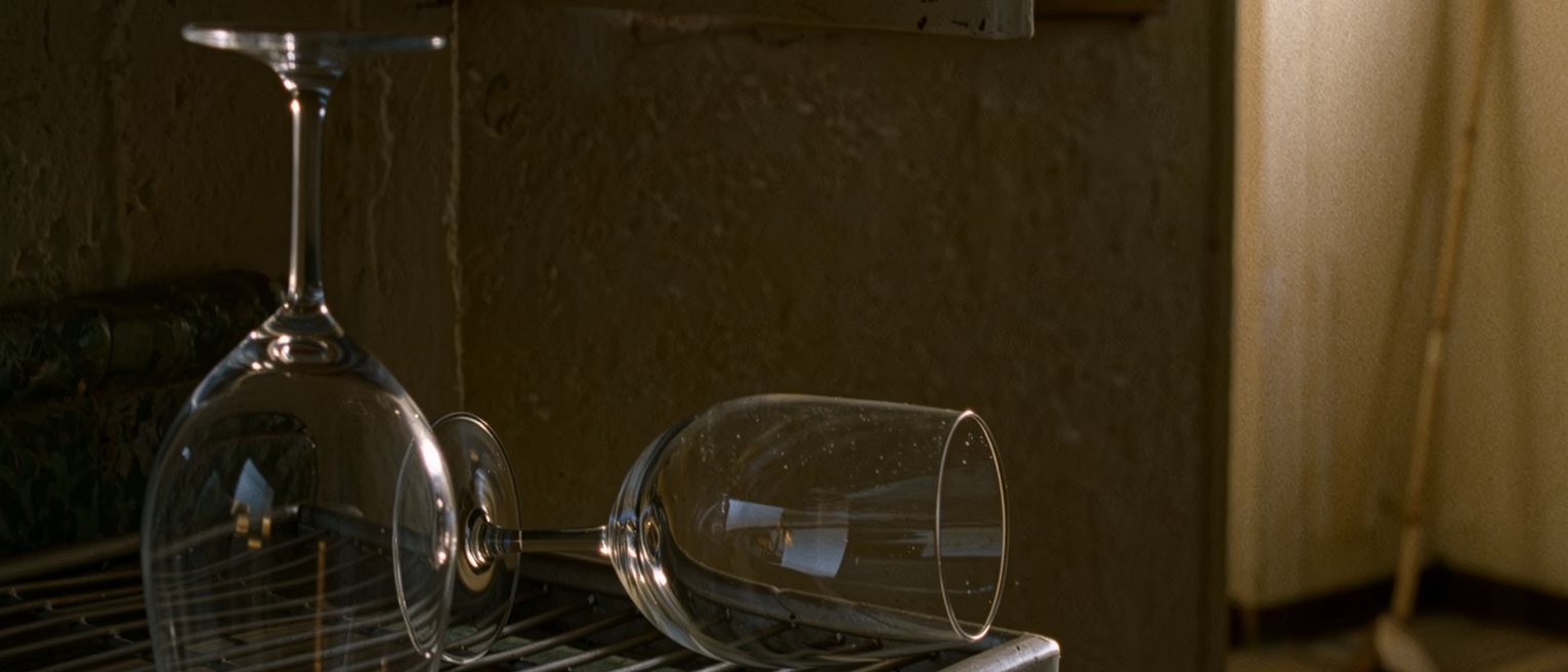 a kitchen with one wine glass washed and upturned on the rack and a second glass, still full, left on the counter