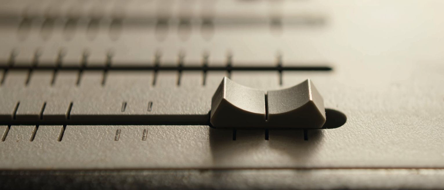 a single mixing desk fader pulled all the way down to its stop and the others left level, the panel beside them smooth and unmarked