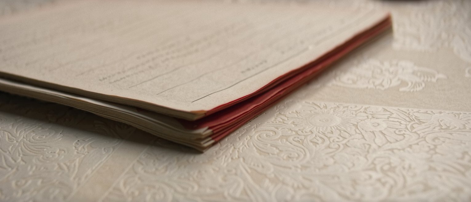 an accounts ledger closed on a desk, the page edges dyed red and the cover worn
