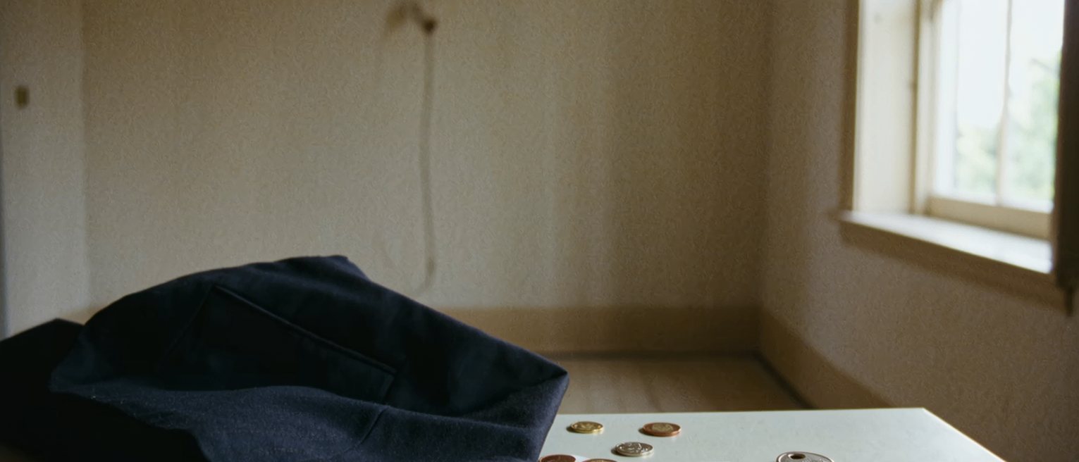 a table seen close with a coat pocket turned out on it, a few coins, a folded receipt and a single key laid in a line beside them