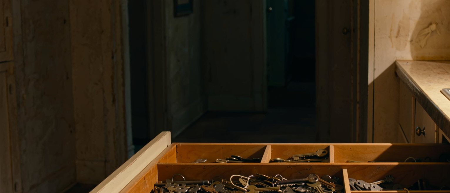 a kitchen drawer pulled open and seen close, one compartment tangled with old keys and cord and the others squared and empty