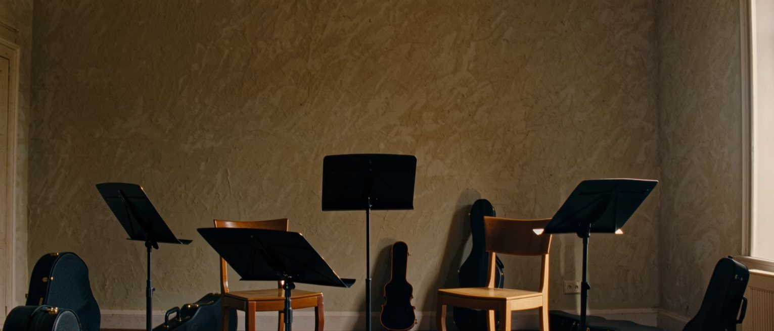 a sitting room with four music stands set in a square, four chairs, and four closed instrument cases of different sizes on the floor beside them