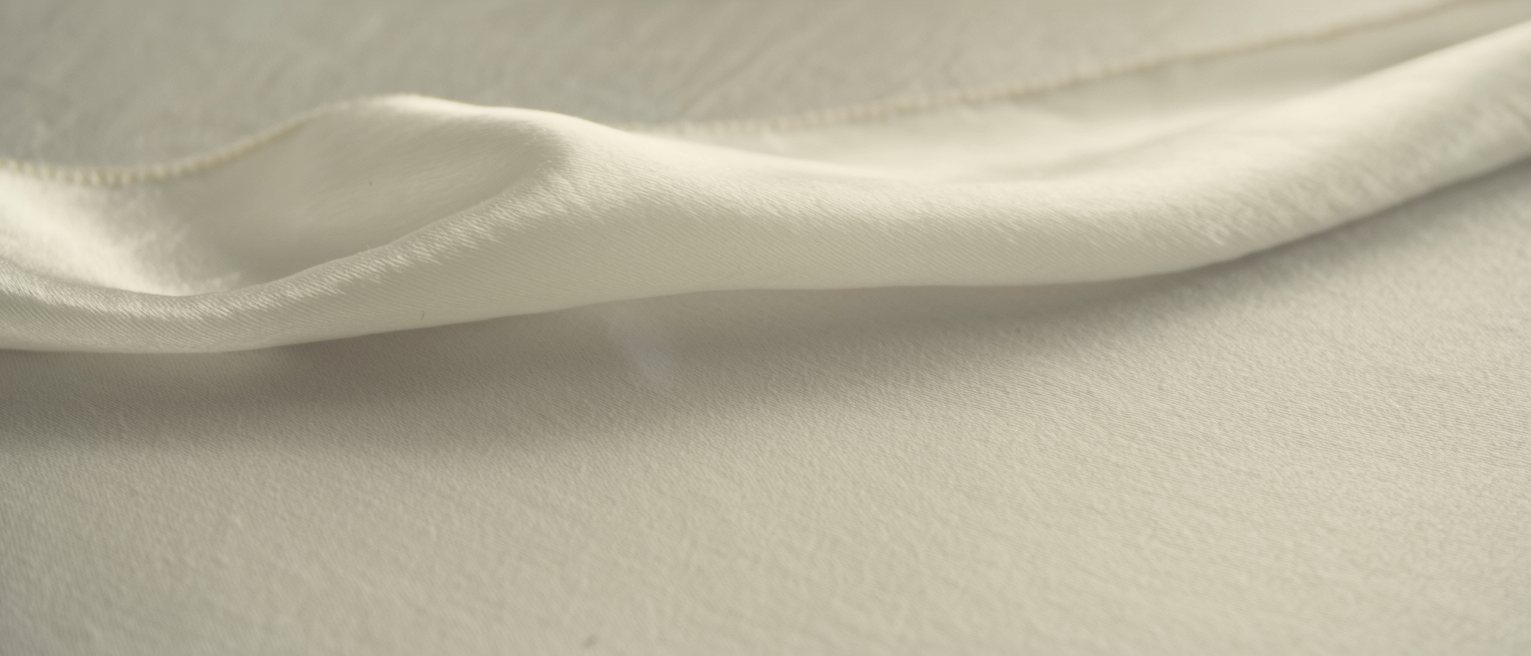 a length of pale silk laid out flat with the light falling full across it, nothing covering it