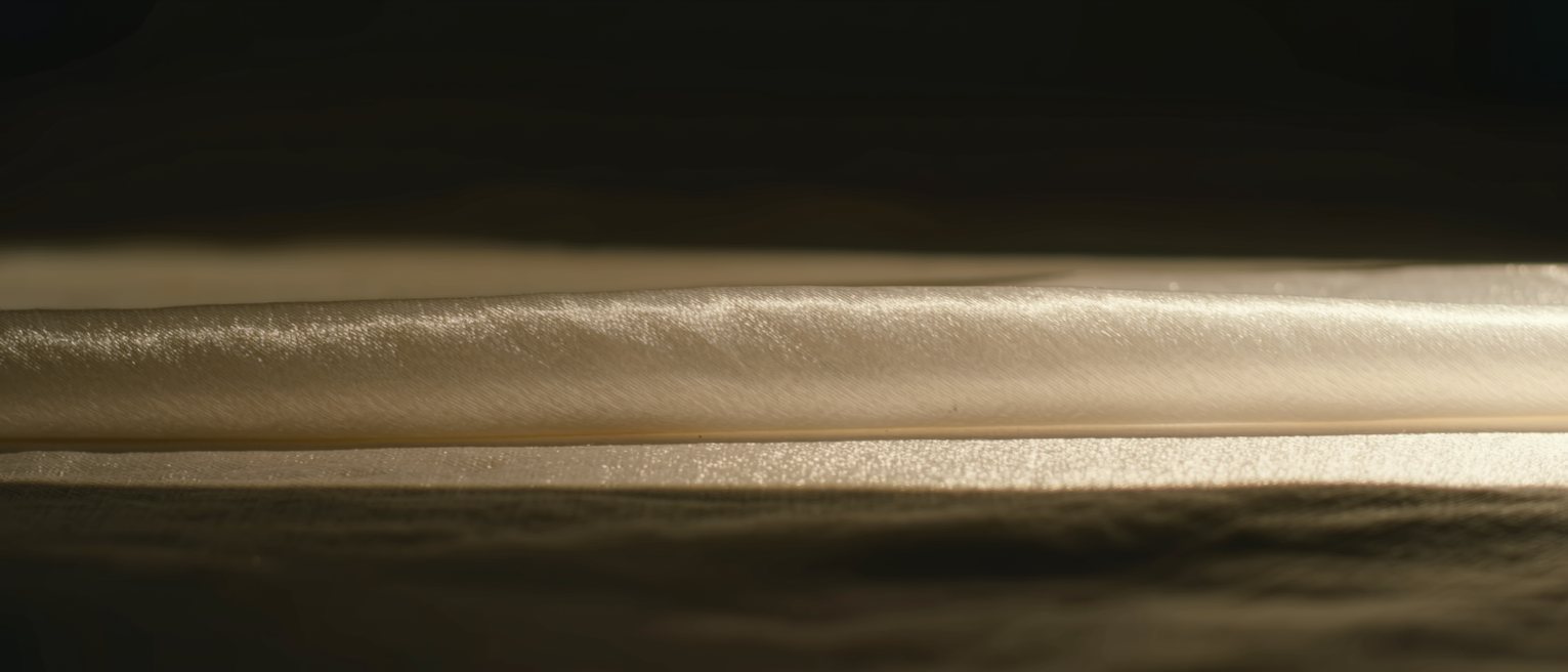 a length of pale silk laid out flat with the light falling full across it, nothing covering it