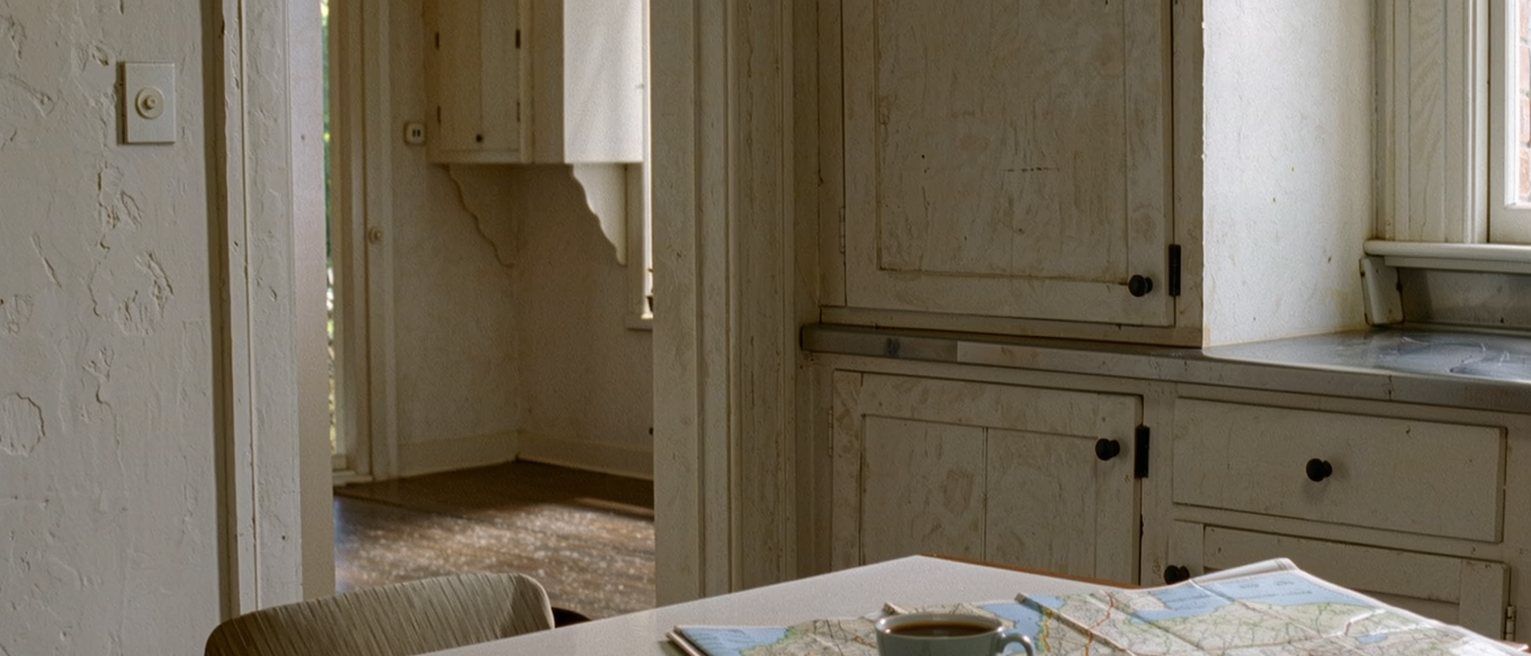 a folded map lying open on a kitchen table with a cup of coffee set down on it, the chair pushed back