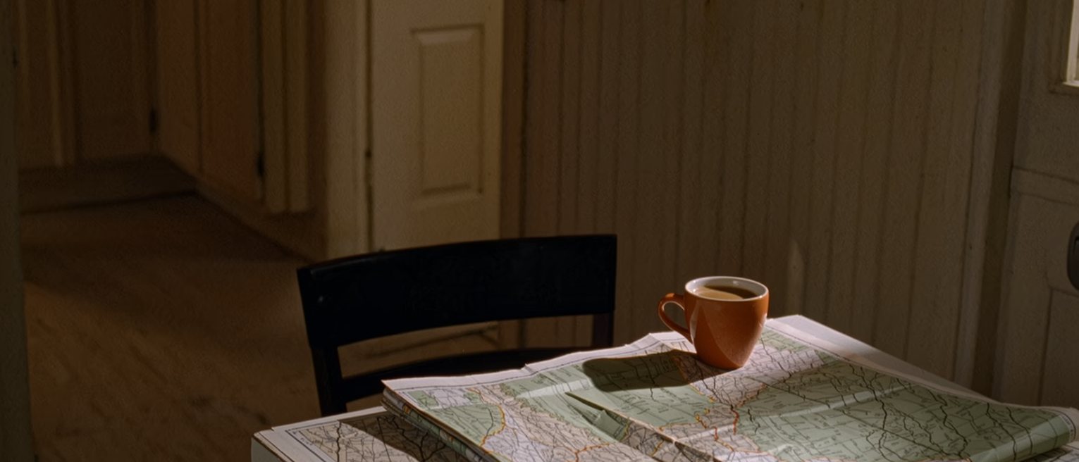 a folded map lying open on a kitchen table with a cup of coffee set down on it, the chair pushed back