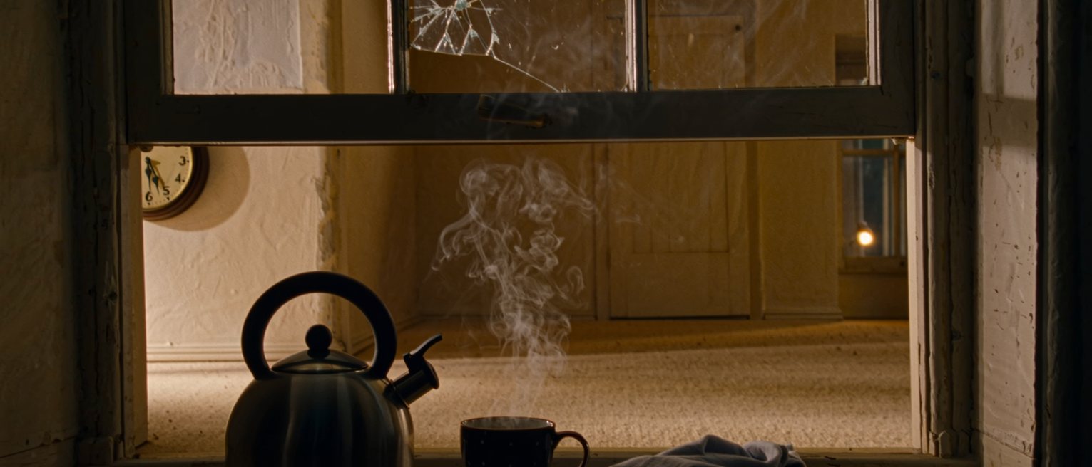 a kitchen seen close with a window cracked open above the counter, a kettle set off the heat with its steam gone, a cup and a folded cloth beside it, a clock on the wall, the room soft beyond