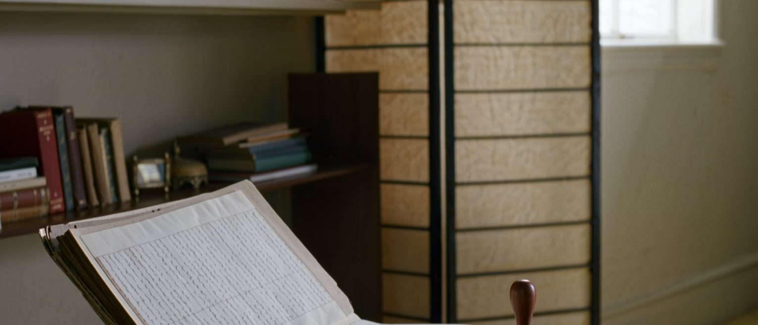 a study seen close with a bound registry ledger open at columns of brush entries, a wooden seal and its red paste, a lacquer box, the shelf close behind and the paper screen soft beyond
